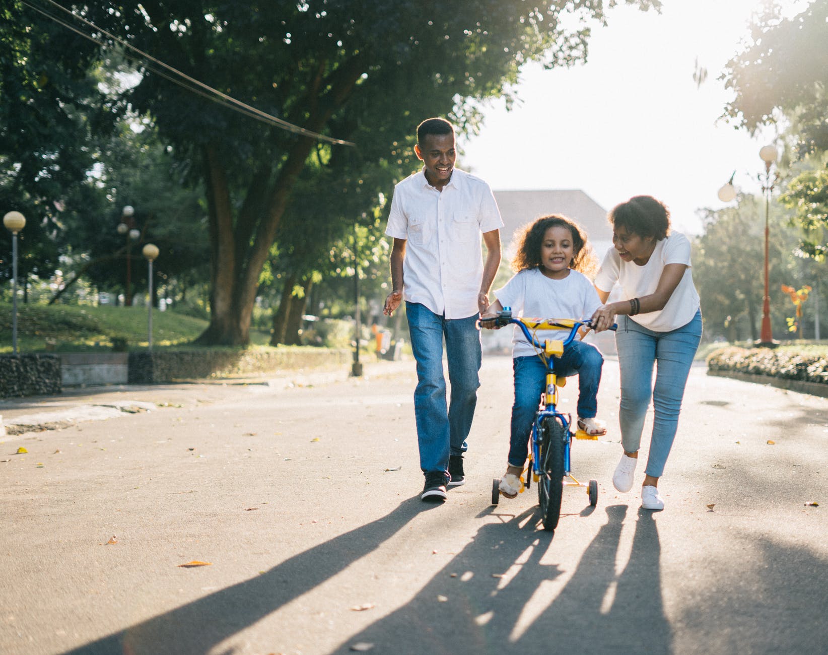 man standing beside his wife teaching their child how to ride bicycle