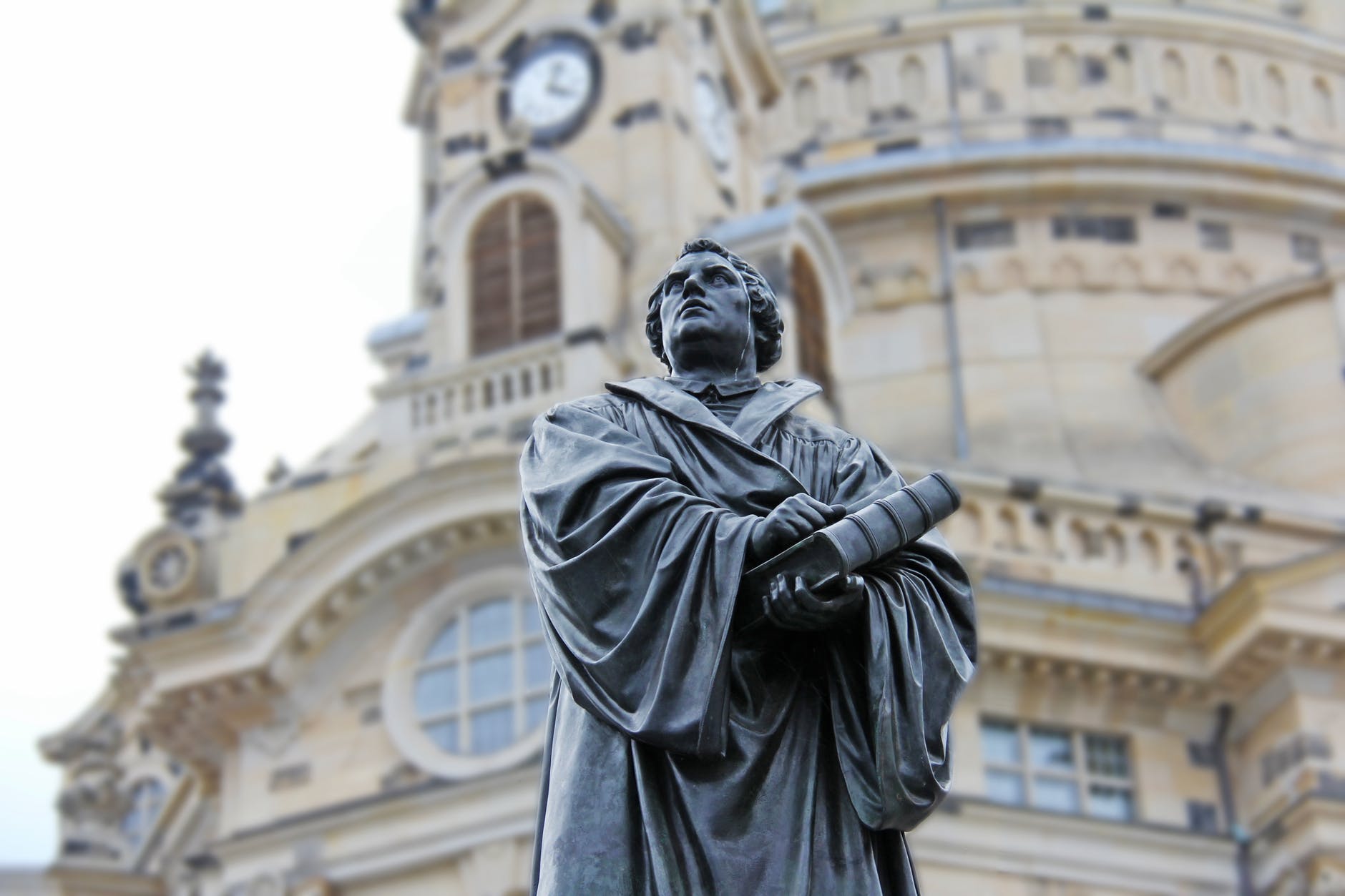 gray concrete statue of man holding book beside brown building